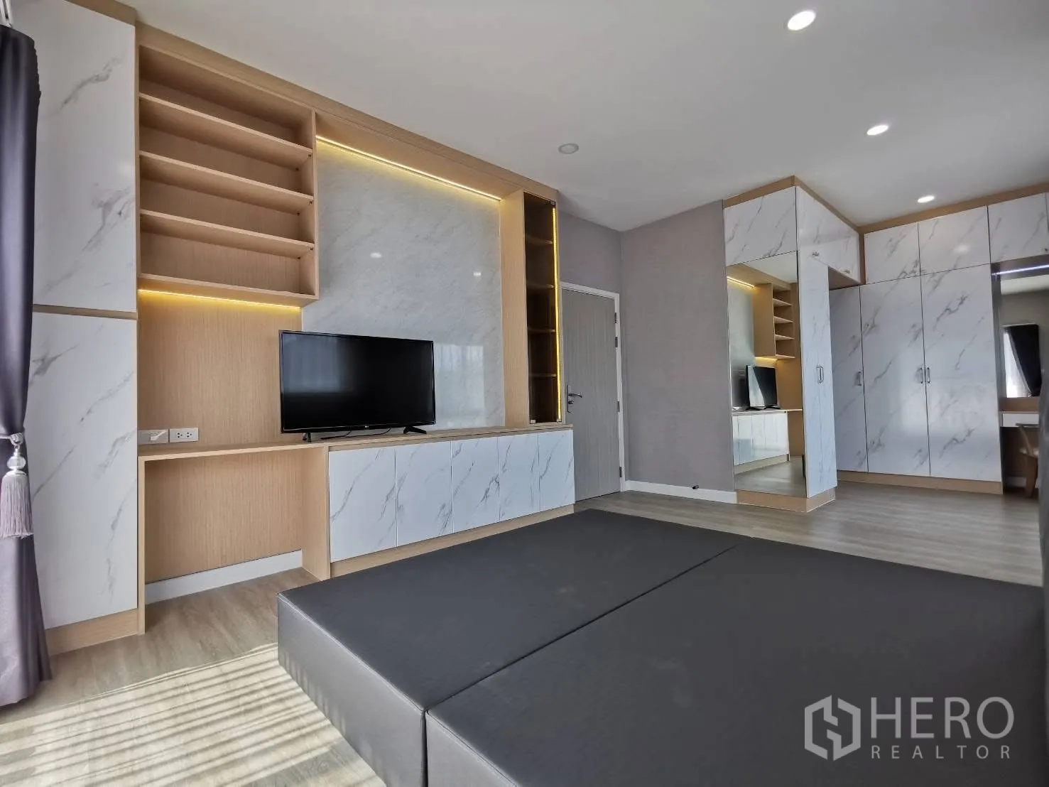 Detached House for rent in Bang Phli, Samut Prakan - Family room featuring extensive built-in cabinetry with LED accents, TV, marble-look panels, and light wood floors.