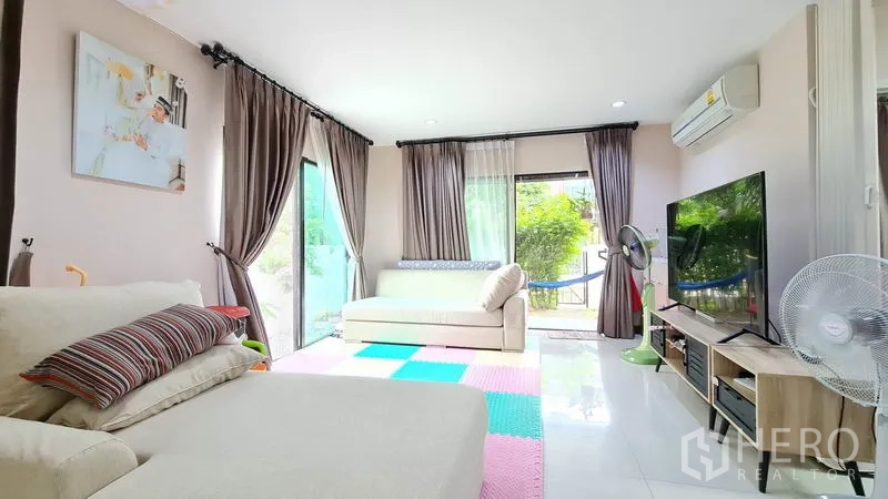 独立式住宅 出售在Samut Prakan - 明亮客厅，沙发与推拉玻璃门，景观面向花园。