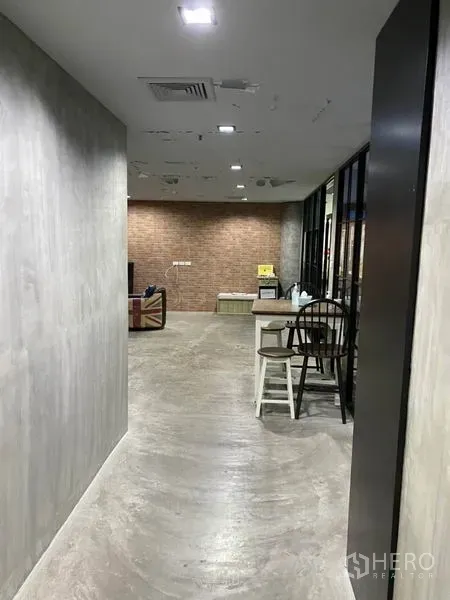 Office Space for rent in Khlong Toei, Bangkok - Industrial-style corridor with concrete walls, recessed ceiling lights and a brick accent lounge area.