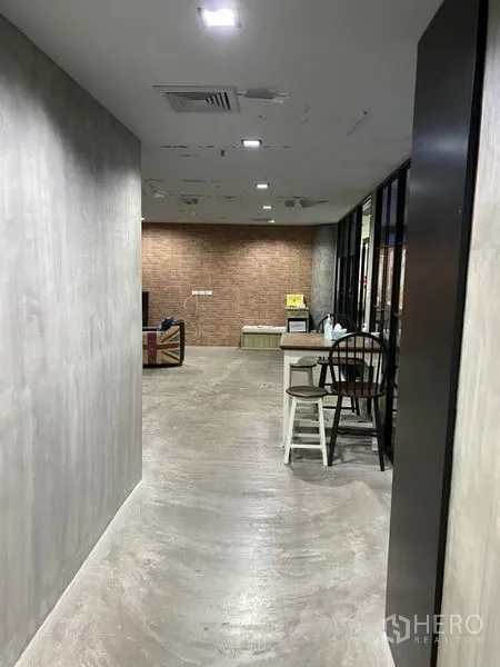 Office Space for rent in Khlong Toei, Bangkok - Industrial-style corridor with concrete walls, recessed ceiling lights and a brick accent lounge area.