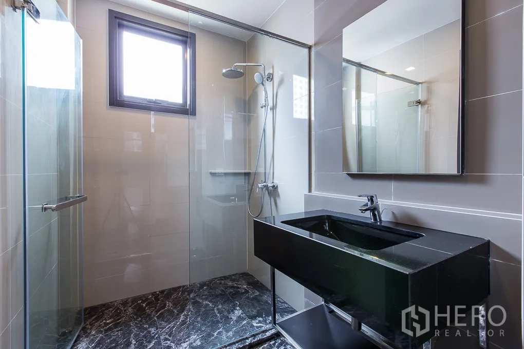 Condominium for rent in Watthana, Bangkok - Glass-enclosed shower with window and sleek black vanity.