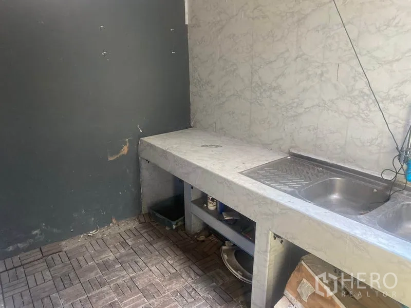 店屋 出租在Watthana, Bangkok - 后方简易厨房，混凝土台面与不锈钢水槽，墙面仿石纹