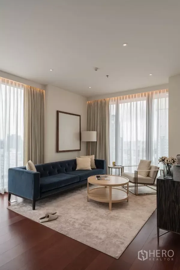 คอนโด ให้เช่าในWatthana, Bangkok - มุมนั่งเล่นรับแสงธรรมชาติ โซฟาสีน้ำเงิน พรมสีอ่อน มองเห็นวิวเมืองผ่านผ้าม่านโปร่ง