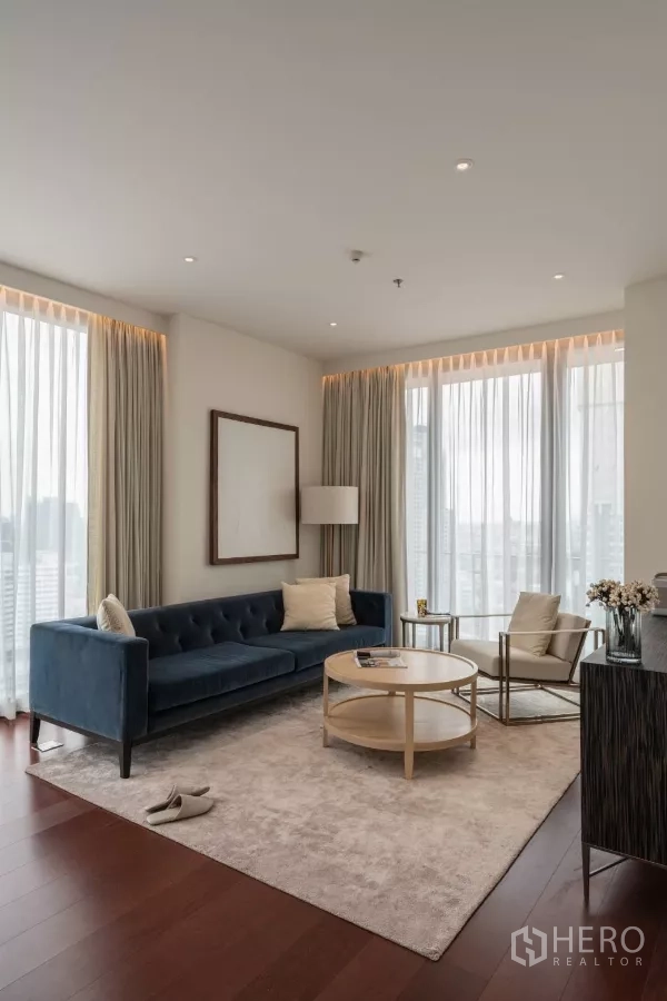 คอนโด ให้เช่าในWatthana, Bangkok - มุมนั่งเล่นรับแสงธรรมชาติ โซฟาสีน้ำเงิน พรมสีอ่อน มองเห็นวิวเมืองผ่านผ้าม่านโปร่ง