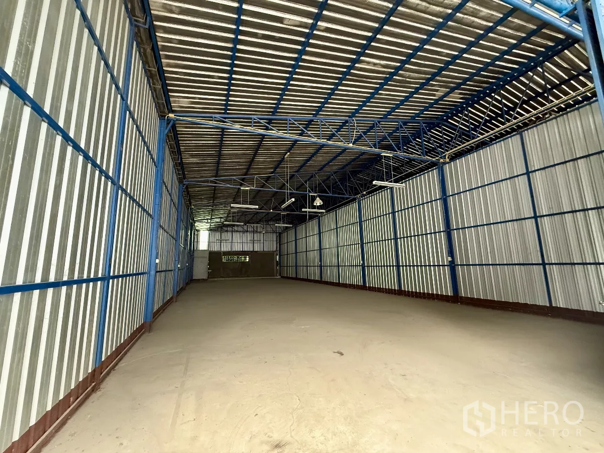 Warehouse for rent in Bueng Kum, Bangkok - Wide-angle view of 290 sqm warehouse showing clear span, corrugated metal walls and hanging lights.