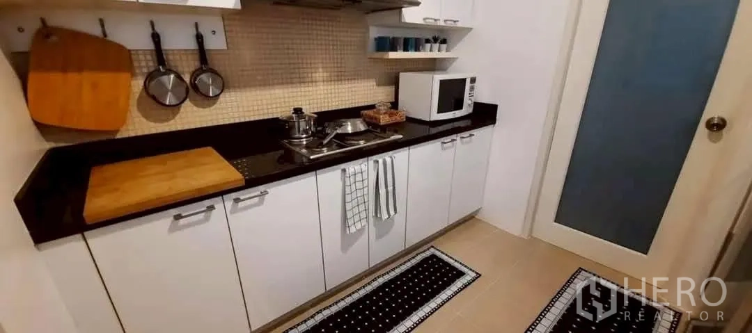 Condominium for rent in Khlong Toei, Bangkok - Compact kitchen with white cabinets, black countertop, microwave and stovetop.