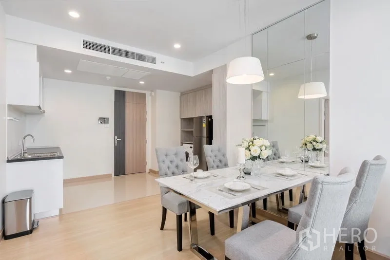 Condominium for sale in Yan Nawa, Bangkok - Compact open kitchen by the dining area, mirrored wall and light wood floors.
