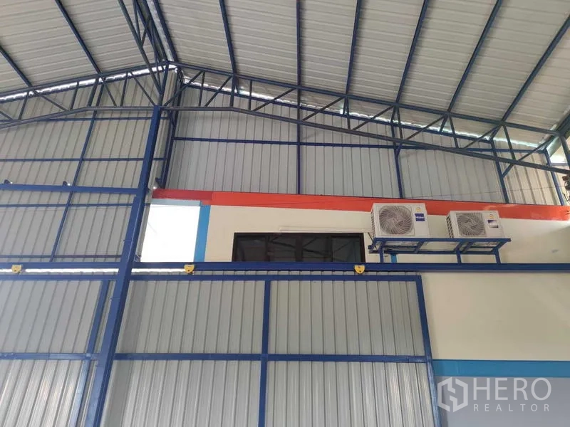 Warehouse for sale in Nakhon Pathom - Close interior wall of the warehouse with blue steel framing, metal cladding and mounted air‑conditioning compressors.