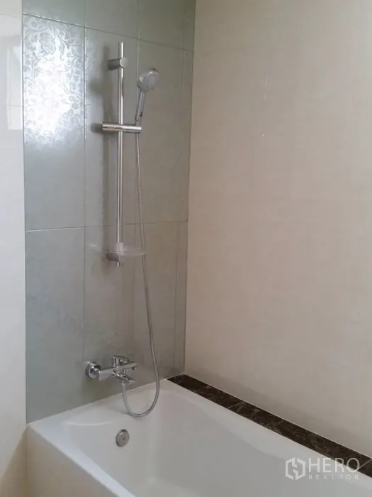 Condominium for rent in Watthana, Bangkok - Bathroom with a white bathtub and handheld shower on a tiled wall.