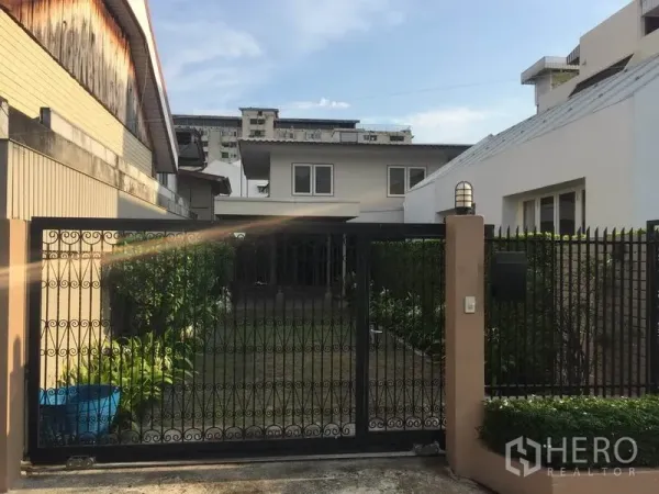 Detached House for rent in Khlong Toei, Bangkok - Front view of a detached house with a wrought-iron gate and a small landscaped lawn.