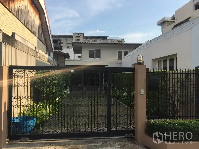 Detached House for rent in Khlong Toei, Bangkok - Front view of a detached house with a wrought-iron gate and a small landscaped lawn.