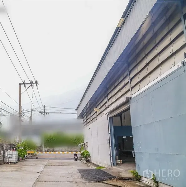 Warehouse for rent in Bang Phli, Samut Prakan - Warehouse exterior with large steel door and wide driveway for truck access on an industrial lane in Bang Phli.