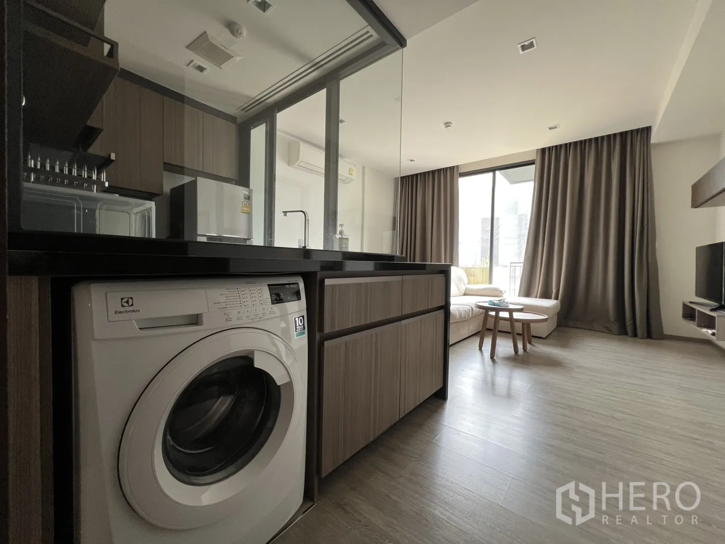 公寓 for rent in Watthana, Bangkok - 开放式起居区，L形沙发、玻璃隔断厨房与嵌入式洗衣机。