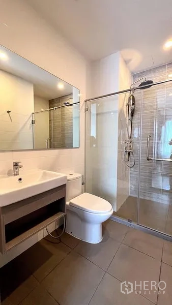 Condominium for rent in Watthana, Bangkok - Modern bathroom with large mirror, vanity, toilet, and glass-enclosed shower.