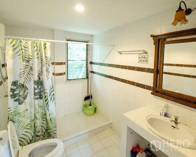 Detached House for sale in Bang Lamung, Chon Buri - Second bathroom with white tiles, vanity, window, and shower area with curtain.
