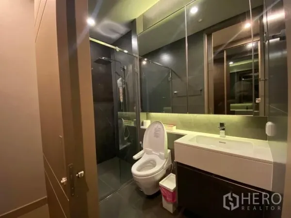 Condominium for rent in Huai Khwang, Bangkok - Contemporary bathroom featuring a glass-enclosed rain shower, wide vanity, and backlit mirror.