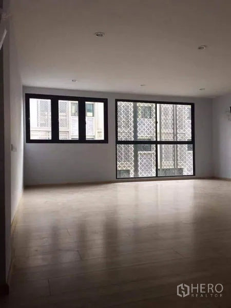 Townhouse for sale in Yan Nawa, Bangkok - Spacious empty room with timber floors and double sets of windows for cross ventilation.