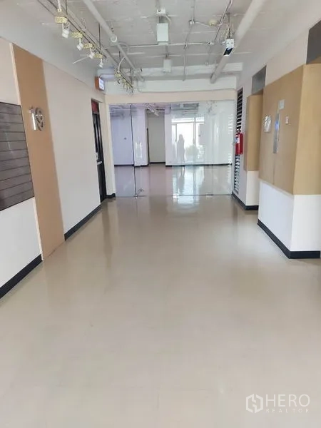 办公空间 出租在Pathum Wan, Bangkok - 办公室走廊明亮，玻璃隔断、吊装灯具与抛光地面。