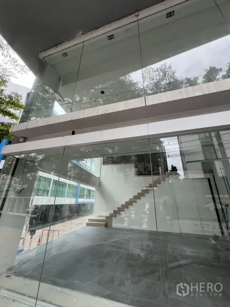 零售空间 出租在Khlong Toei, Bangkok - 宽幅玻璃店面，展示开放式空间与通往夹层的楼梯。