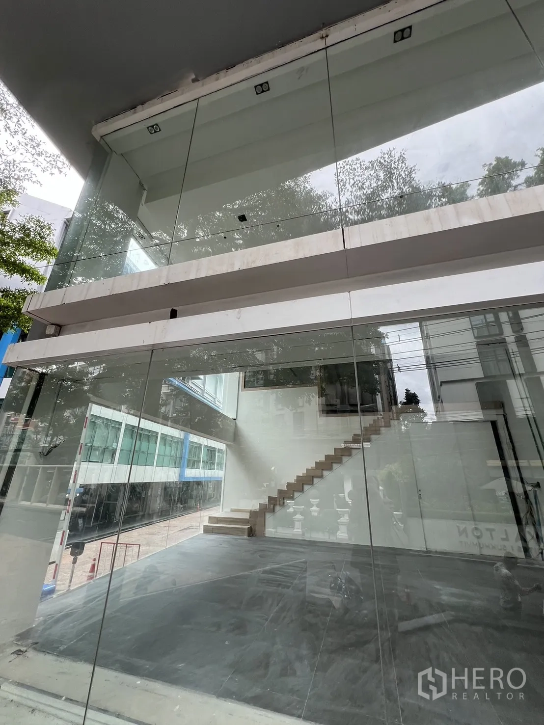 零售空间 出租在Khlong Toei, Bangkok - 宽幅玻璃店面，展示开放式空间与通往夹层的楼梯。