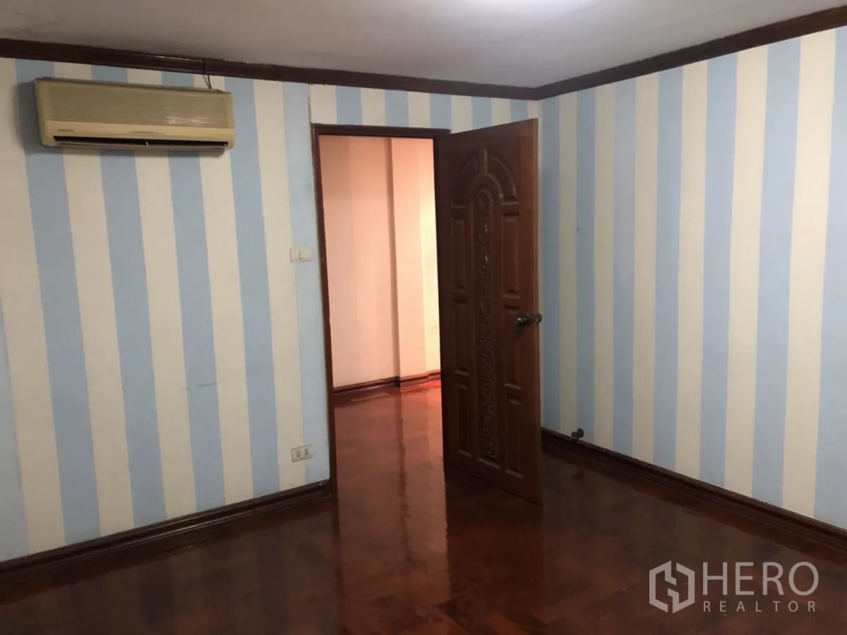 สำนักงานที่บ้าน ให้เช่าในPhra Khanong, Bangkok - ห้องนอนผนังลายทางฟ้า‑ขาว ประตูไม้ และแอร์แขวนผนัง