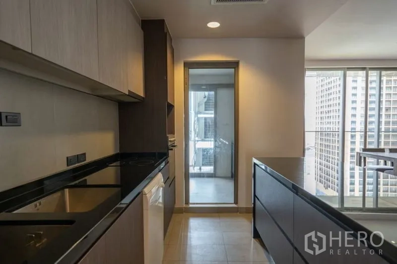 คอนโด ให้เช่าในKhlong Toei, Bangkok - ครัวกะทัดรัดท็อปหินสีดำ มีไอส์แลนด์และประตูสู่ระเบียงบริการ มองเห็นตึกสูง