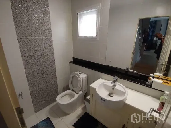 Detached House for sale in Khlong Sam Wa, Bangkok - Modern bathroom with white tiles, mosaic accent wall, window, mirror, and vanity basin.