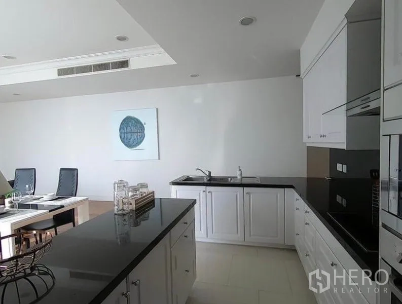 Condominium for rent in Watthana, Bangkok - U-shaped white kitchen with black stone countertops, built-in oven and center island.