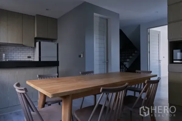 联排别墅 出租在Watthana, Bangkok - 餐区设长木桌和椅子，毗邻开放式欧式厨房。