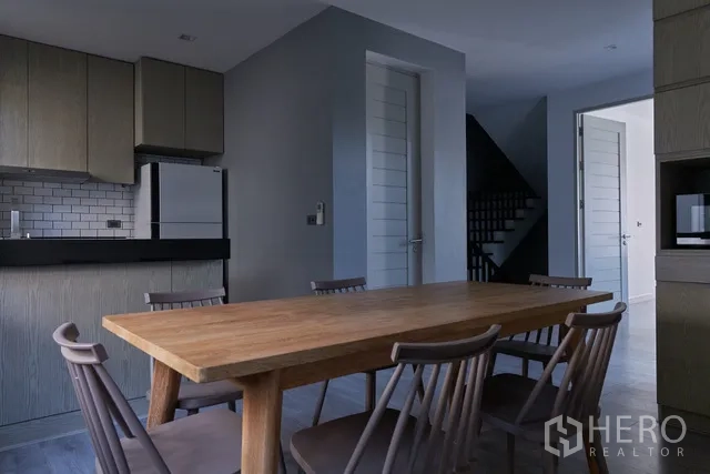 联排别墅 出租在Watthana, Bangkok - 餐区设长木桌和椅子，毗邻开放式欧式厨房。