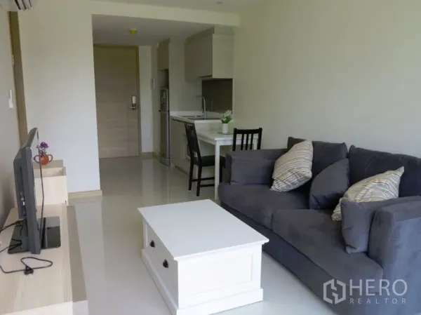 คอนโด ให้เช่าหรือขายในWatthana, Bangkok - พื้นที่นั่งเล่นแบบเปิดโล่งพร้อมครัวขนาดกะทัดรัด เคาน์เตอร์ทานข้าว และโซฟาสีเทา ในคอนโด 1 ห้องนอน