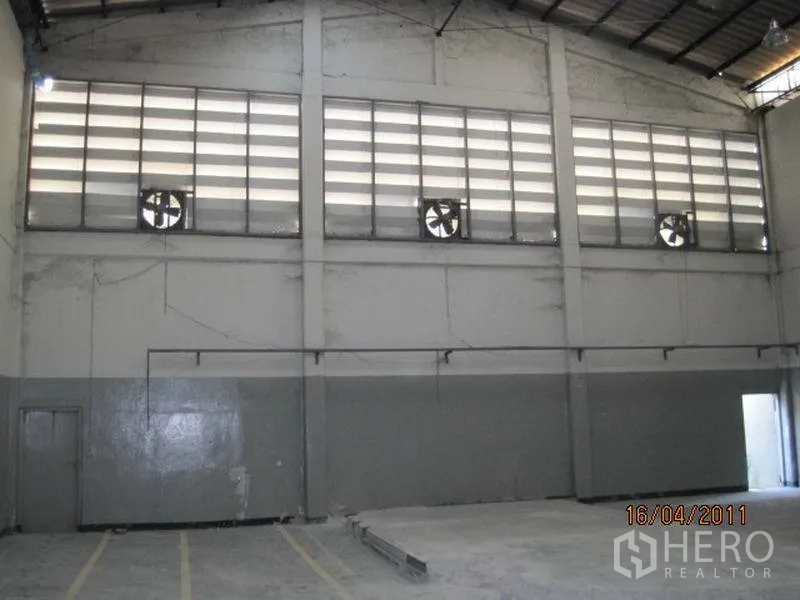 Factory for rent in Bang Sao Thong, Samut Prakan - High-ceiling factory hall with louvered windows, exhaust fans, and a concrete floor.