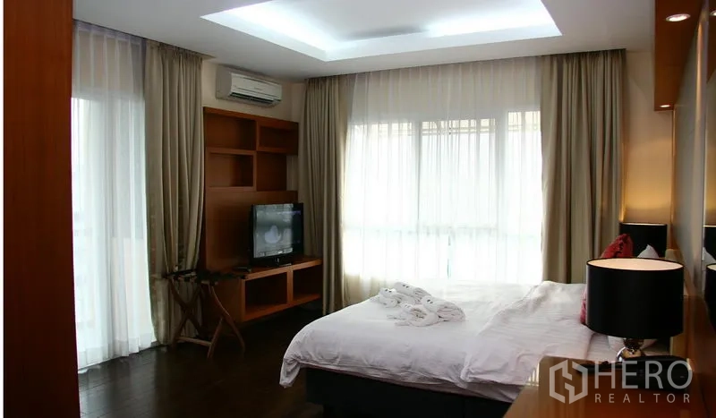 Apartment for rent in Khlong Toei, Bangkok - Bright master bedroom with large curtains, TV console and a sliding door to the exterior
