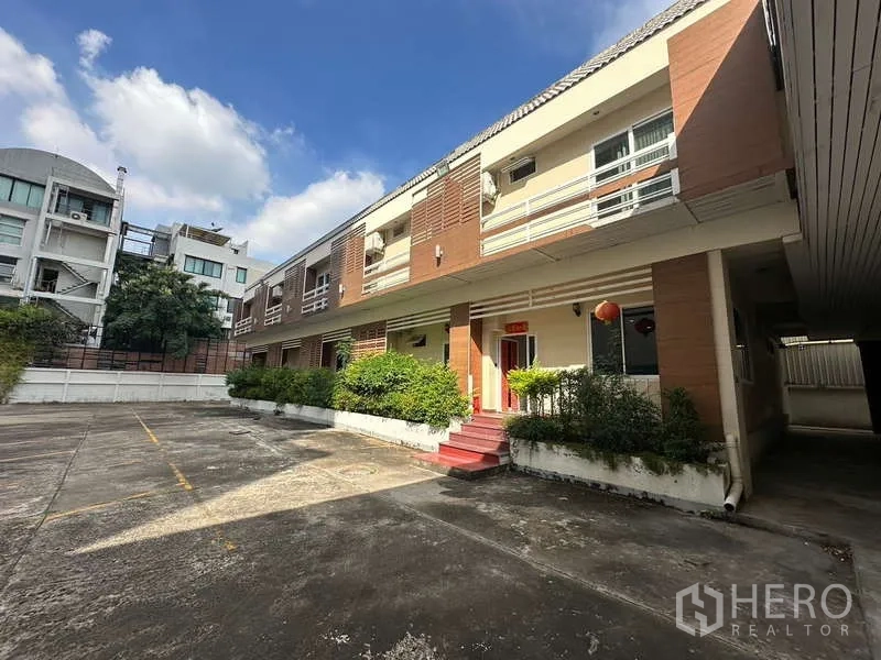 Home Office for rent in Chatuchak, Bangkok - Low-rise building exterior with parking courtyard and landscaped shrubs.