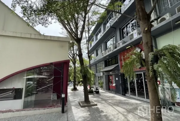 店屋 出租在Wang Thonglang, Bangkok - 树荫步道旁的低层商业建筑与玻璃店面。