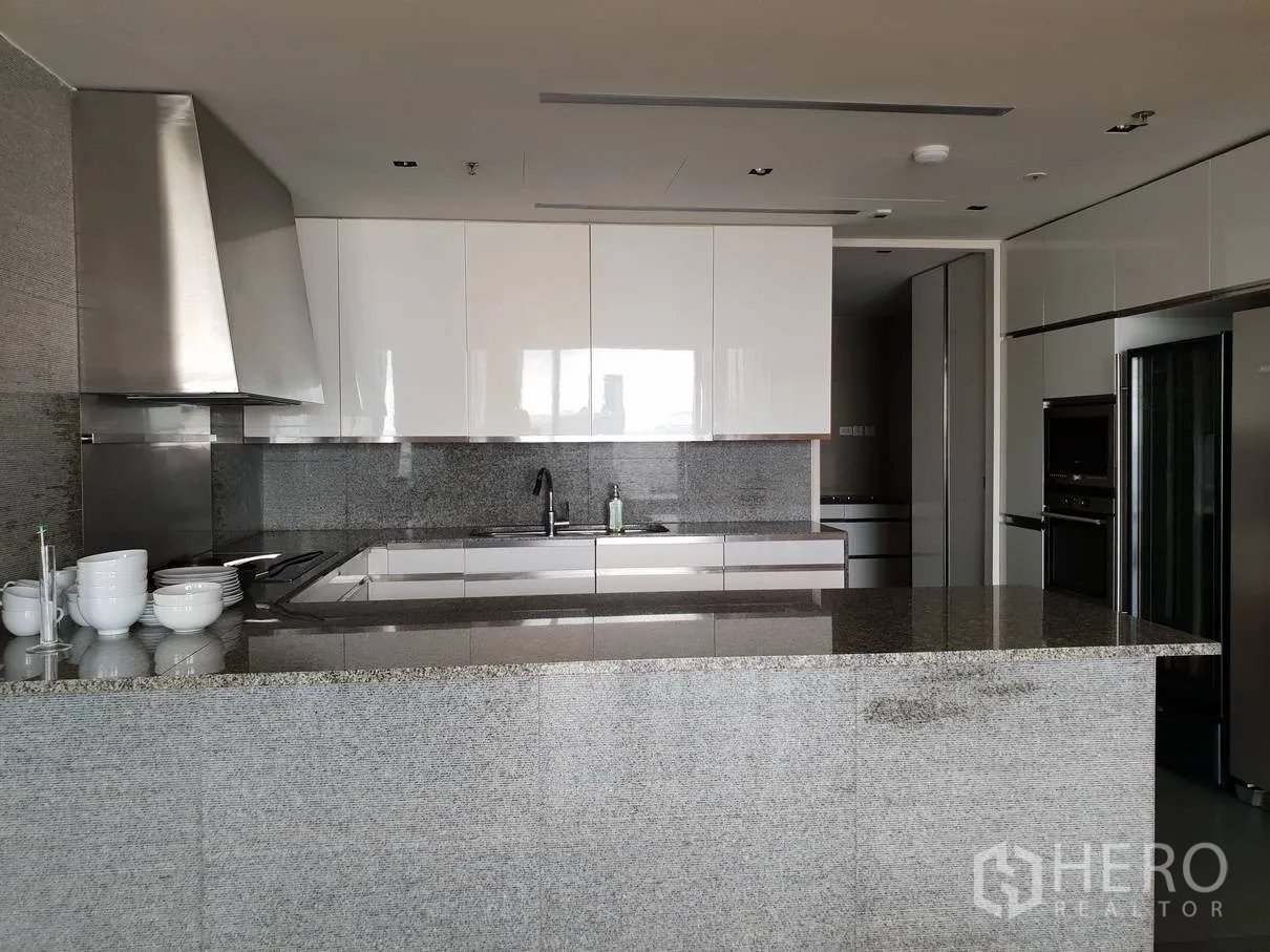 Condominium for rent in Sathon, Bangkok - Modern kitchen with a large granite island, glossy white cabinets, stainless range hood and built-in appliances.