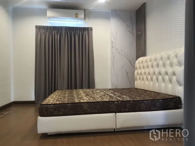 Detached House for rent in Prawet, Bangkok - Bedroom with white tufted bed, air conditioner and gray curtains.