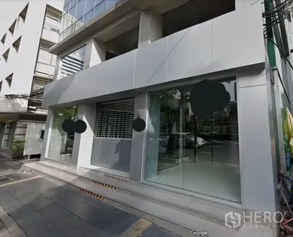 零售空间 出租在Bang Rak, Bangkok - 是隆区现代商业楼外立面，带大面积玻璃橱窗、卷闸门与街道台阶入口。