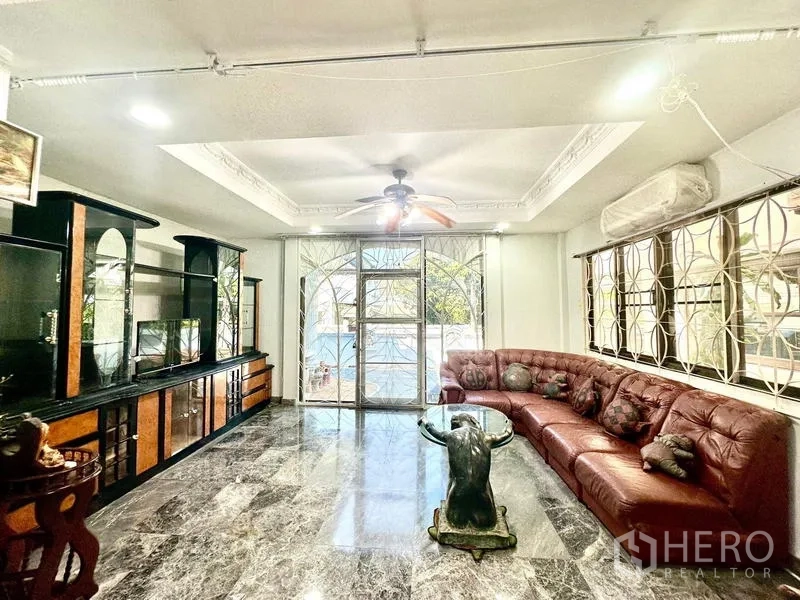 บ้าน ให้เช่าในTaling Chan, Bangkok - ห้องพักผ่อนพร้อมโซฟาหนังรูปตัวแอล ตู้โชว์บิลท์อิน พัดลมเพดาน และประตูกระจกสไลด์ออกชานบ้าน.