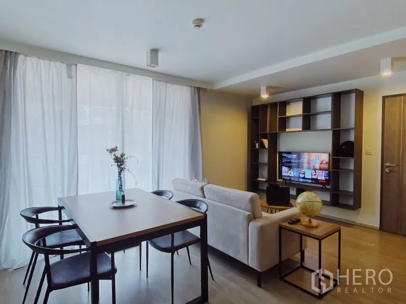 คอนโด ให้เช่าในPathum Wan, Bangkok - พื้นที่นั่งเล่นและรับประทานอาหารสว่างด้วยผ้าม่านโปร่ง โซฟา โต๊ะสี่ที่นั่ง และชั้นวางบิลท์อินพร้อมทีวี