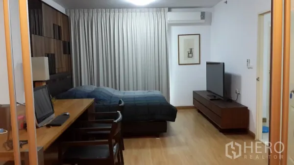 คอนโด ให้เช่าในHuai Khwang, Bangkok - พื้นที่นั่งเล่น-นอนพื้นไม้ โทนอบอุ่น พร้อมเตียง โต๊ะทำงานยาว ตู้วางทีวี ผ้าม่าน และเครื่องปรับอากาศ