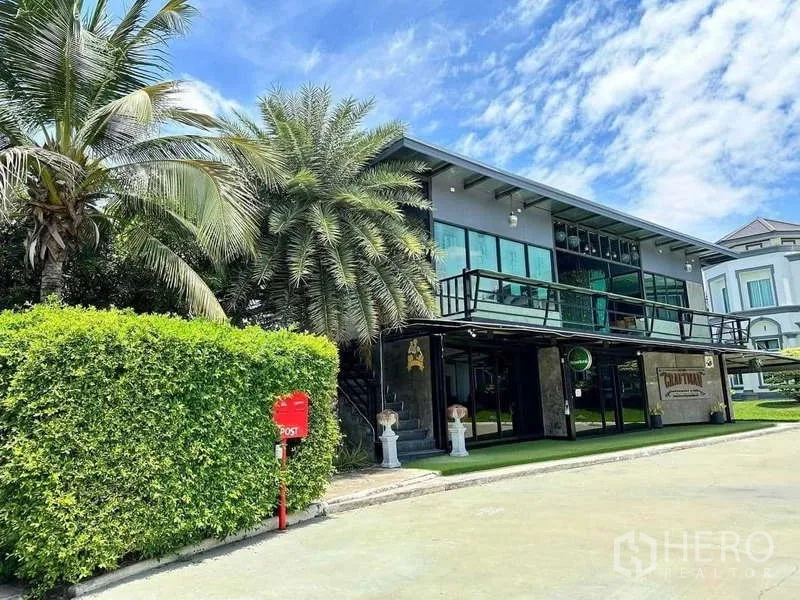 บ้าน ขายในKhlong Luang, Pathum Thani - อาคารอเนกประสงค์สมัยใหม่พร้อมระเบียงรอบอาคาร ข้างต้นปาล์มและแนวพุ่มไม้