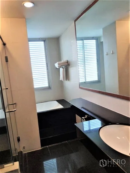 Condominium for rent in Bang Rak, Bangkok - Bathroom with wide mirror, countertop sink, bathtub and separate glass shower enclosure.