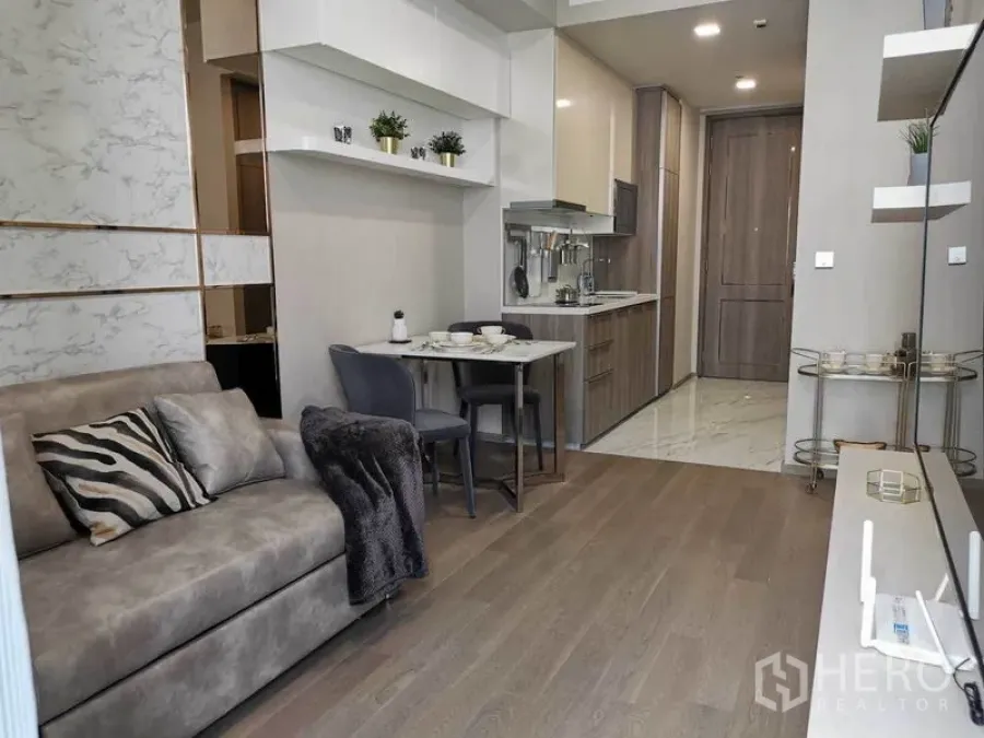 Condominium for rent in Watthana, Bangkok - Compact dining nook and fitted kitchenette facing the entry hall, with wood flooring and soft lighting.
