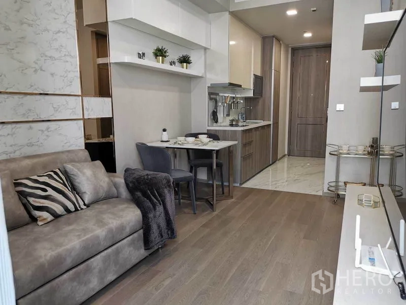 Condominium for rent in Watthana, Bangkok - Compact dining nook and fitted kitchenette facing the entry hall, with wood flooring and soft lighting.