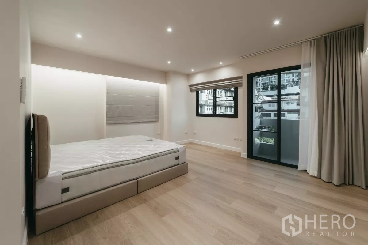联排别墅 出租在Watthana, Bangkok - 宽敞卧室，木地板，推门通阳台与柔和窗帘。