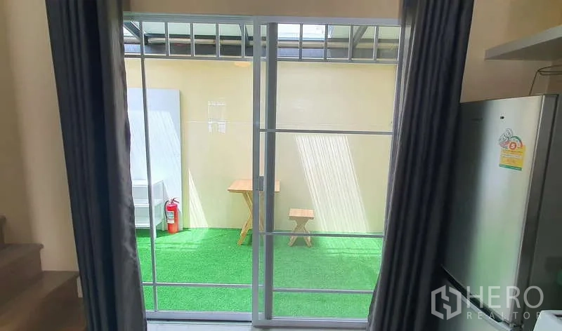 独立式住宅 出租在Bang Phli, Samut Prakan - 透过推拉门可见带顶人造草坪露台与小桌椅。