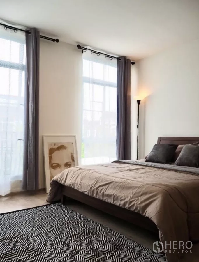 Townhouse for rent in Bang Phli, Samut Prakan - Sunlit master bedroom with double bed, tall windows, curtains and a floor lamp.