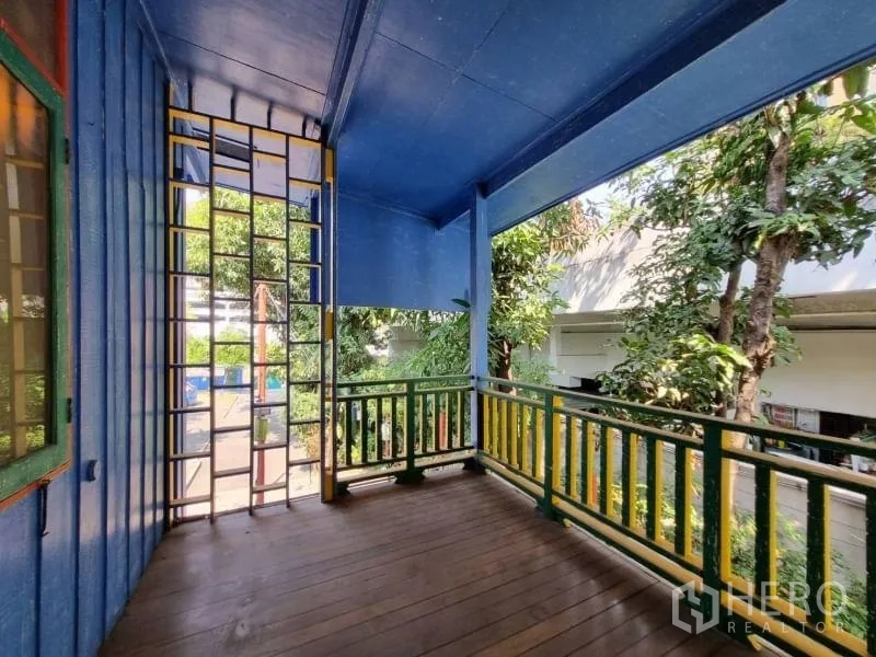 Detached House for rent in Khlong Toei, Bangkok - Covered balcony with wooden floor and green-and-yellow railings overlooking trees.