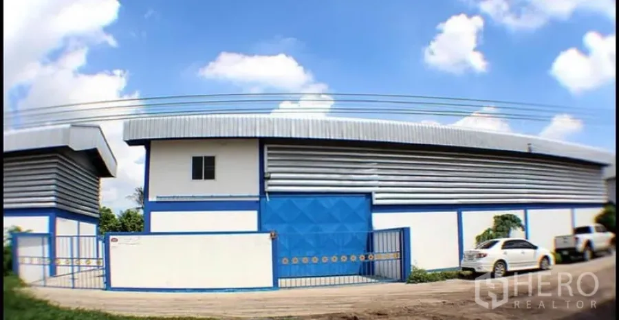 工厂 出租在Pak Kret, Nonthaburi - 蓝白色工厂外立面，金属屋顶，宽滑动大门与道路旁停车位